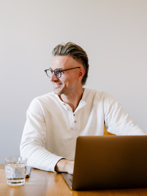 Mann sitzt vor dem Laptop und blickt fröhlich nach rechts.